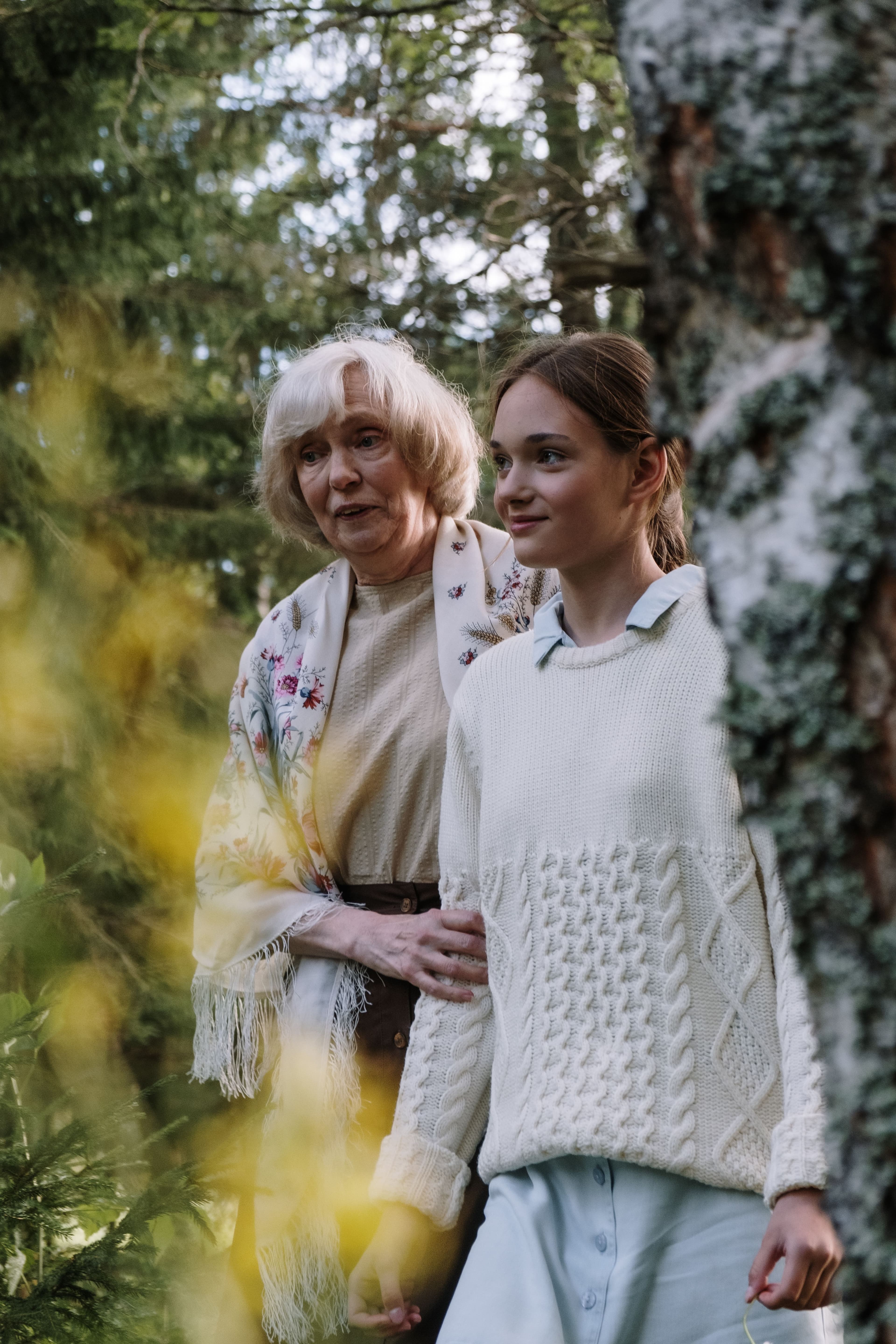 En eldre og en yngre kvinne står tett sammen mellom trærne