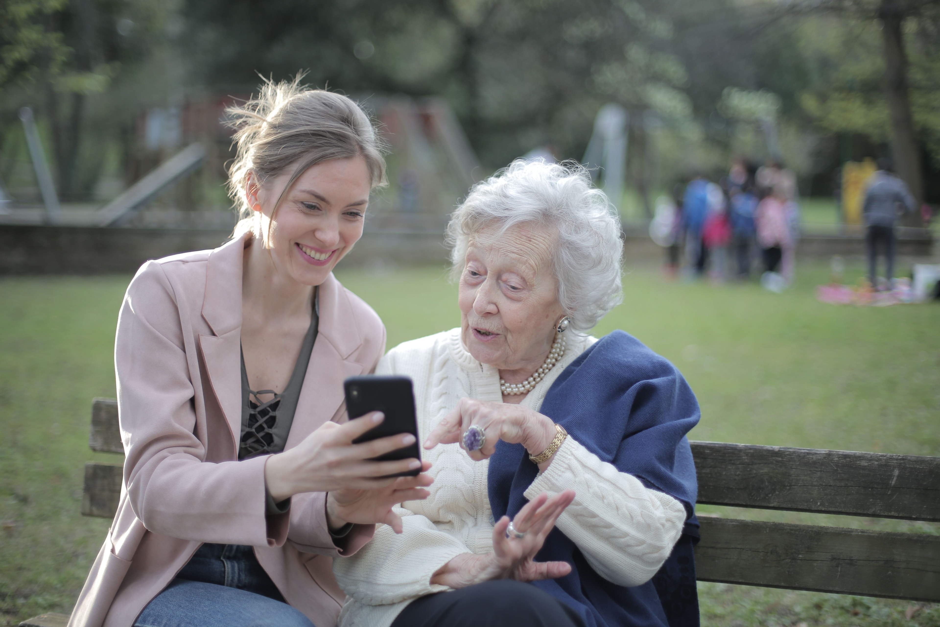 To kvinner ser på en mobiltelefon sammen på en benk i en park